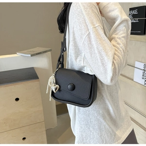 Detail of black lychee grain saddle bag with pearl heart charm and round buckle strap