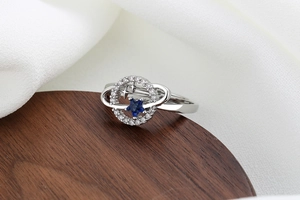 Macro detail of silver star ring with blue center gem and pavé crystals on a wooden stand