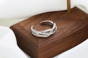 Macro view of triple-braided silver twist open ring on a dark wooden display stand
