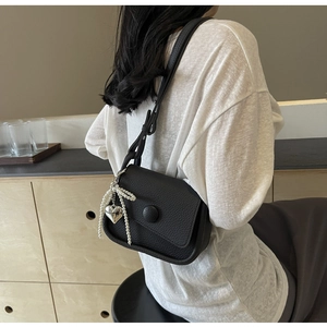 Detail of black lychee texture saddle bag with pearl bow and silver heart pendant