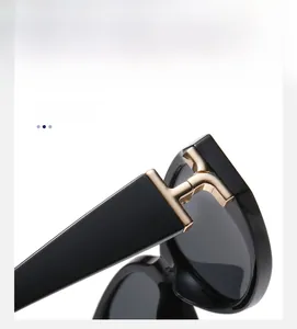 Detail of sleek black sunglasses featuring a distinctive golden T-shaped metal hinge inlay