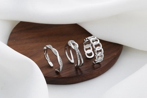 Dettaglio di un set di tre anelli in argento con design a catena e intrecciato su legno
