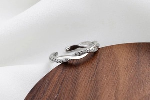 Dettaglio anello aperto intrecciato argento con pietre lucide su fondo in legno