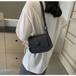 Close-up of black lychee grain saddle bag with pearl and heart pendant tassel charm