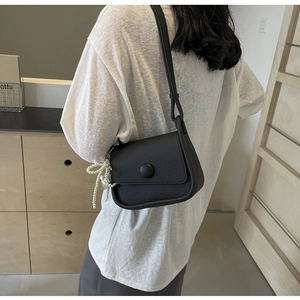 Detail view of black lychee grain saddle bag featuring a stylish pearl bead charm and round buckle