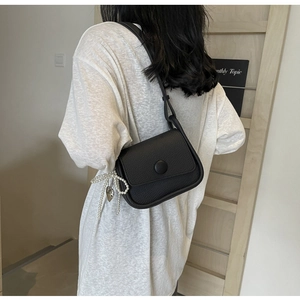 Detail of black lychee grain leather saddle bag with pearl bow and heart charm