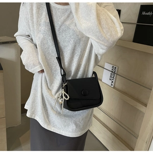 Close-up of black lychee grain leather saddle bag with pearl heart charm on a shoulder strap