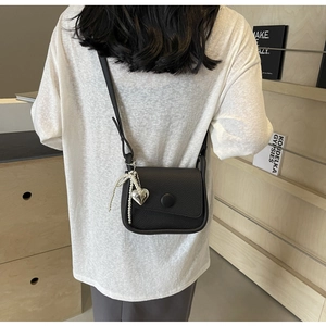 Detail of black lychee leather saddle bag with pearl heart pendant and flap closure