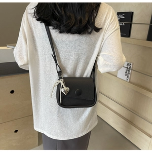 Detail view of black litchi pattern saddle bag with heart charm and pearl accents