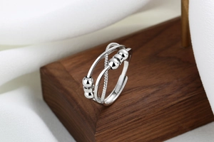 Detail of silver multi-layer crossover ring with beads on wood and silk background