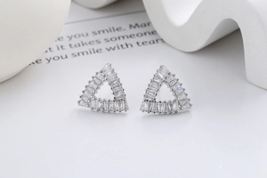 Macro view of silver triangle stud earrings with rectangular zircon stones on white base