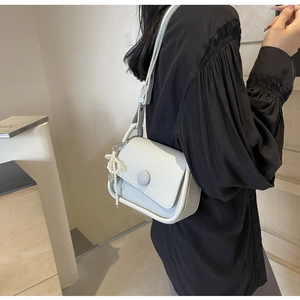 Detail of grey lychee leather saddle bag with round buckle and pearl bow charm