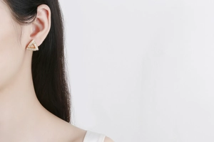 Detail of model wearing gold triangular stud earrings inlaid with cubic zirconia stones