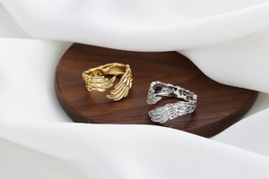 Detailed close-up of gold and silver feather-shaped adjustable rings on wood base