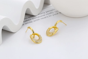 Detail of gold double-hoop earrings with pave-set zircon stones on a minimalist stand