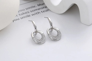 Detail of silver oval earrings with micro-set zircons on a minimalist background