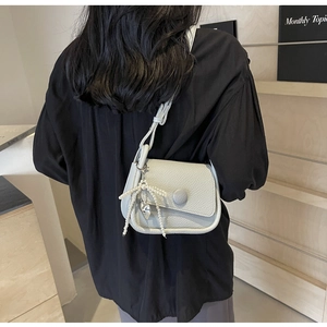 Detail of light gray lychee grain saddle bag with pearl bow charm and heart pendant