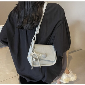 Detail of light gray lychee grain leather saddle bag with pearl bow charm on black shirt
