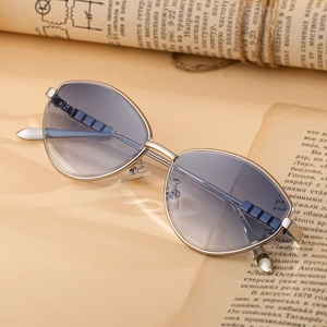 Occhiali da sole cat-eye vintage con montatura in metallo argento e lenti blu sfumate su libri