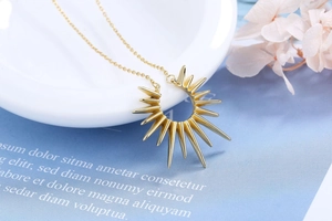 Detail der 18K vergoldeten Sonnenanhänger-Kette auf hellblauem Hintergrund