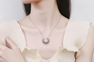 Detailaufnahme einer silbernen Sonnenanhängerkette mit Strahlen auf dem Hals eines Models