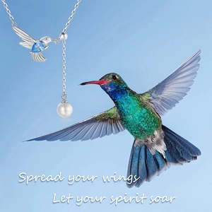 Macro detail of hummingbird necklace featuring blue teardrop stone and white round pearl