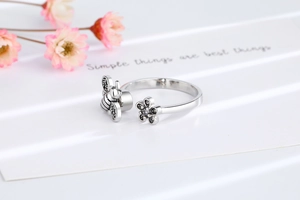Macro detail of rotating bee and daisy open ring with black pavé stones on white texture