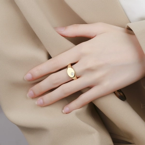 Minimalist gold signet ring with engraved starburst and diamond on index finger
