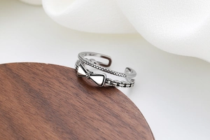 Gros plan d'une bague nœud argentée vintage sur bois sombre et satin blanc