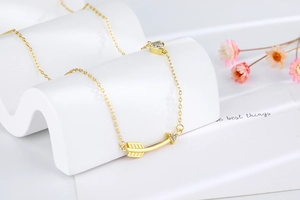 Detail of gold arrow necklace with heart gem on a white textured display stand