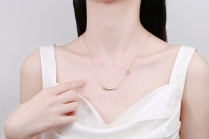 Detail of minimalist gold arrow pendant necklace with heart charm on female collarbone