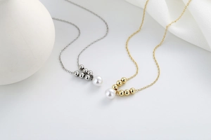 Detail of minimalist gold and silver necklaces featuring polished metal beads and white pearls