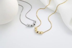 Detail of gold and silver box chains with five textured geometric beads on fabric