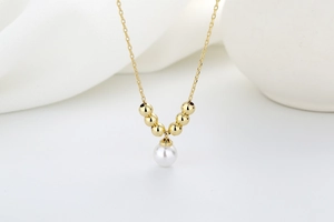 Detail of gold necklace featuring six golden beads and a white pearl pendant