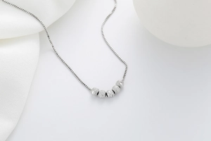 Detailed shot of silver s925 box chain necklace with five textured beads on white silk