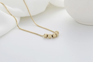 Macro detail of a gold necklace featuring five frosted beads on a delicate box chain