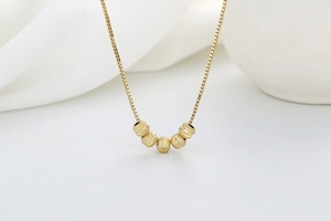 Detailed macro view of golden box chain with five frosted beads on white silk fabric