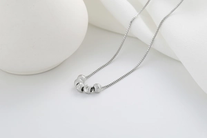 Detailed view of silver box chain necklace with five frosted beads on white silk