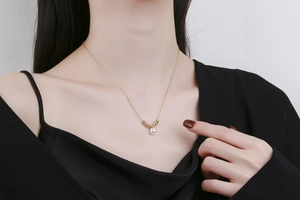 Close-up of a minimalist gold pearl necklace worn on a collarbone with a black top