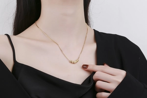 Detail of gold necklace with five textured beads on a delicate chain worn on collarbone