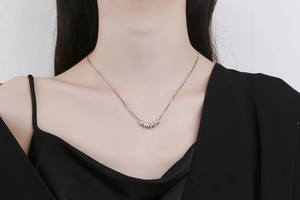 Close-up of minimalist silver five-bead clavicle necklace on model with black outfit