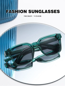 Detail view of square green transparent sunglasses with grey lenses on a reflective surface