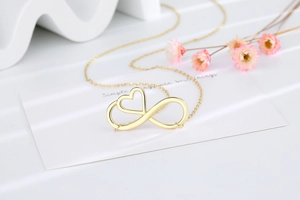 Close-up of golden infinity heart necklace on a white display card with pink flowers