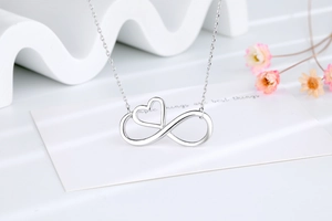 Detailed close-up of a silver infinity heart pendant necklace on a minimalist display