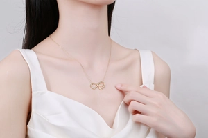 Detail of infinity heart pendant necklace worn by model on silk blouse for elegant look