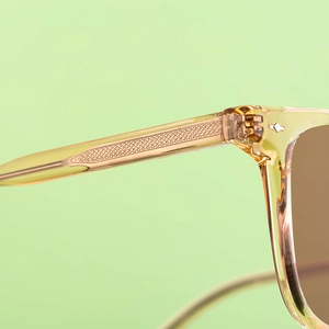 Detail of yellow transparent sunglasses frame featuring engraved metal wire core inside temple