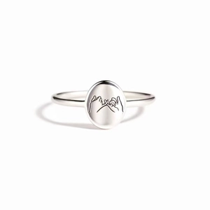Macro detail of silver ring featuring engraved pinky swear hand gesture on oval face
