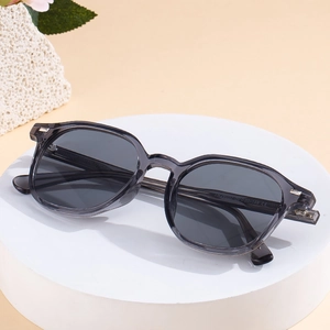 Lunettes de soleil rétro avec monture grise transparente sur un support minimaliste