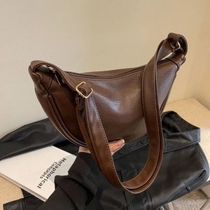Detail view of smooth dark brown crescent bag texture with a metallic buckle adjustment