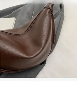 Close-up of brown crescent bag with premium lychee grain texture and zipper detail